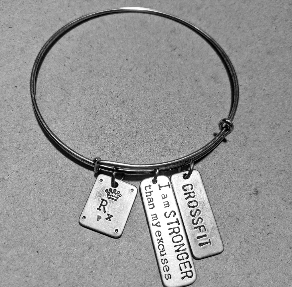 Stainless Steel bracelet with three charms has a crown with the letters RX, second charm says I am stronger than my excuses, and third charm says crossfit